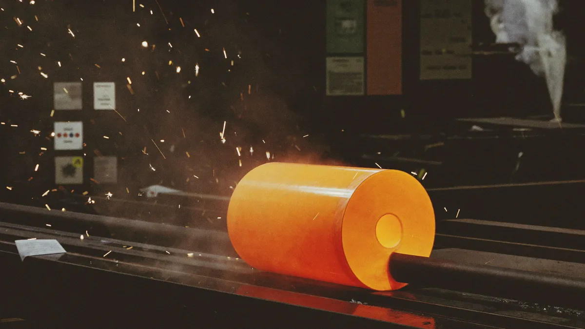 Billetta d'acciaio incandescente su una linea di laminazione, con scintille e vapore
